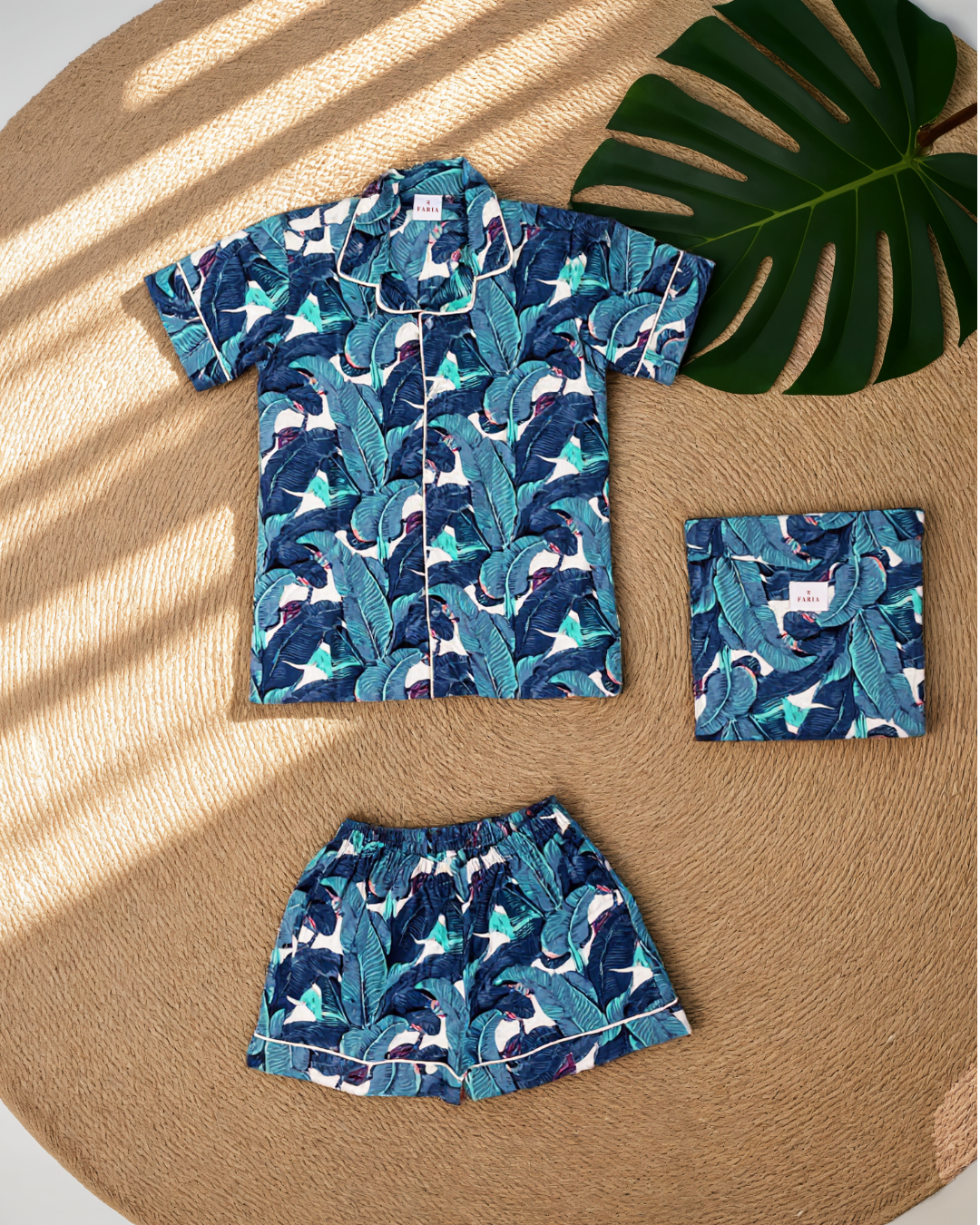 N Faria Blue Leaf Luxe PJ Set shirt and shorts styled on a wooden table with tropical leaf.
